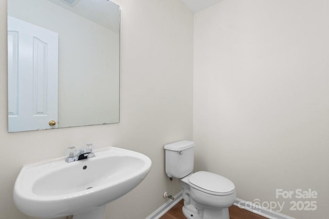 half bath with toilet, baseboards, a sink, and wood finished floors