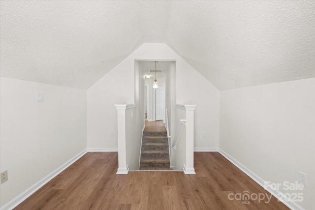 additional living space featuring a textured ceiling, baseboards, wood finished floors, and lofted ceiling