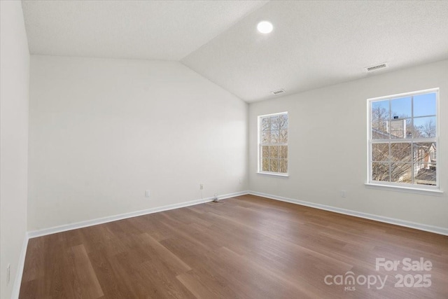 spare room with a textured ceiling, wood finished floors, visible vents, baseboards, and vaulted ceiling