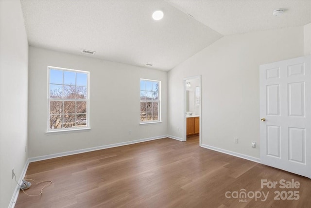 unfurnished bedroom featuring baseboards, visible vents, lofted ceiling, wood finished floors, and a textured ceiling