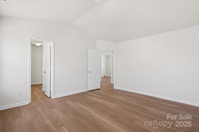 unfurnished bedroom featuring light wood-type flooring, a walk in closet, lofted ceiling, and baseboards