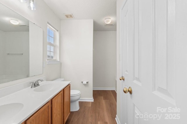 full bath with a textured ceiling, toilet, wood finished floors, visible vents, and a sink