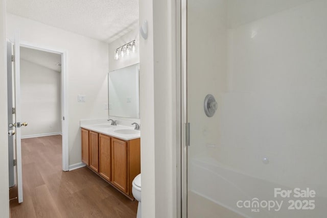 bathroom featuring a textured ceiling, wood finished floors, a stall shower, and a sink