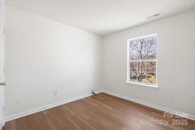 spare room featuring a textured ceiling, plenty of natural light, wood finished floors, and visible vents