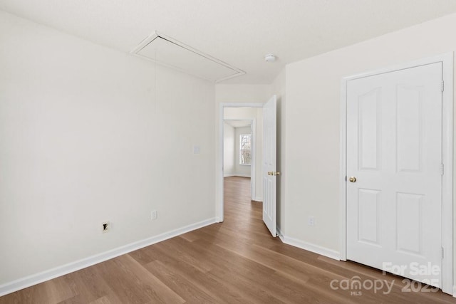 unfurnished bedroom featuring wood finished floors, attic access, and baseboards