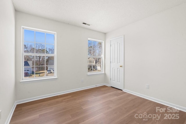 empty room featuring baseboards, a textured ceiling, visible vents, and wood finished floors