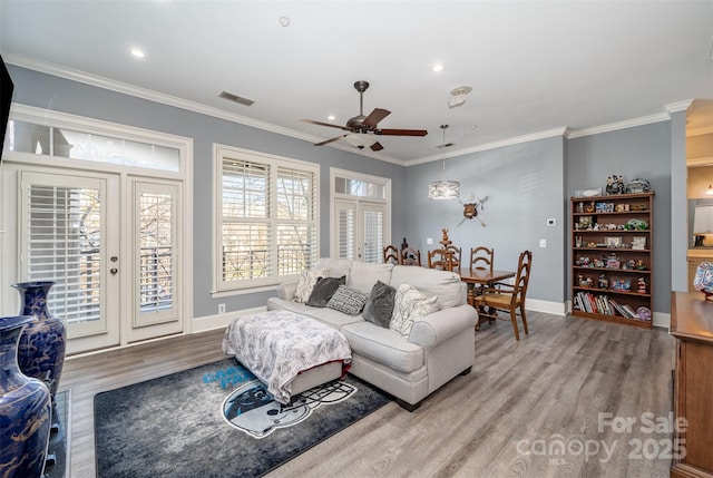 living area with french doors, crown molding, visible vents, wood finished floors, and baseboards