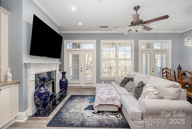 living room featuring a fireplace with flush hearth, visible vents, crown molding, and light wood-style flooring