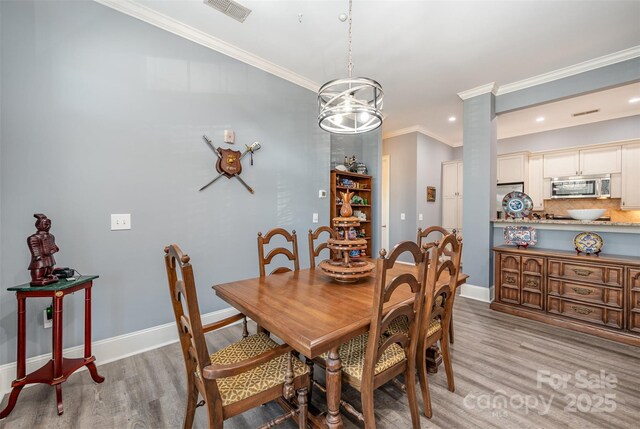 dining space featuring baseboards, light wood-style flooring, visible vents, and crown molding