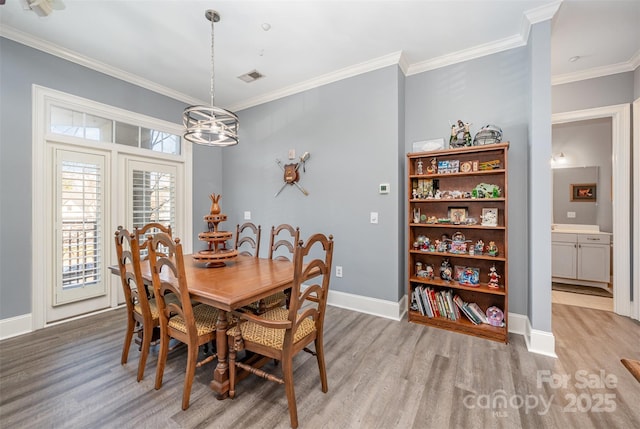 dining area with light wood-style floors, visible vents, and crown molding