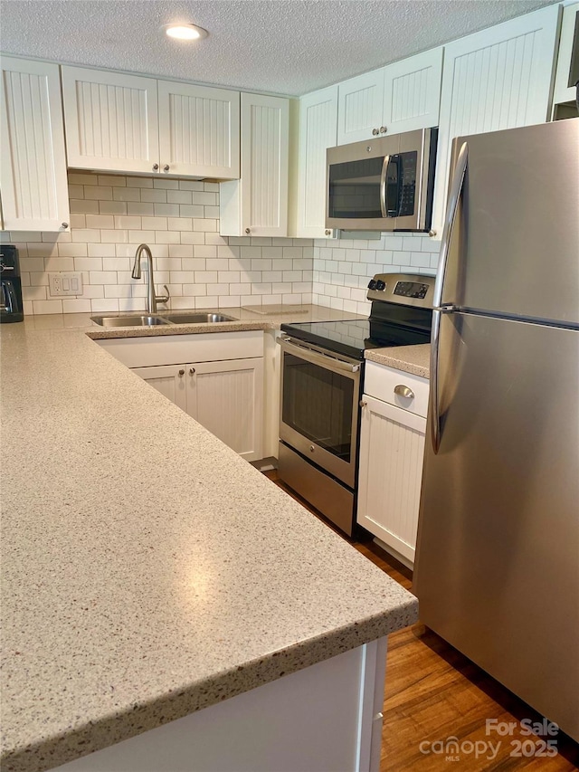 kitchen featuring decorative backsplash, appliances with stainless steel finishes, dark wood-style floors, a textured ceiling, and a sink