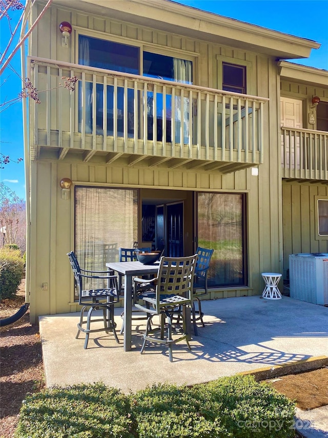 rear view of house featuring outdoor dining space, a balcony, a patio area, and board and batten siding