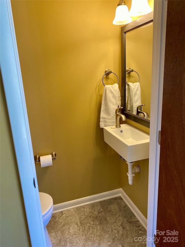 half bath with a sink, baseboards, and toilet