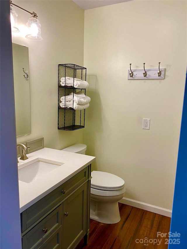 half bathroom with vanity, toilet, wood finished floors, and baseboards