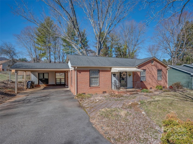 ranch-style house with a shingled roof, aphalt driveway, an attached carport, crawl space, and brick siding