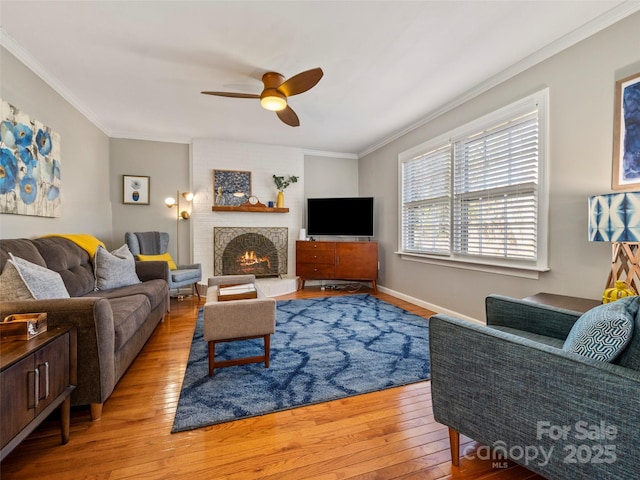 living area with light wood finished floors, a fireplace, a ceiling fan, and crown molding