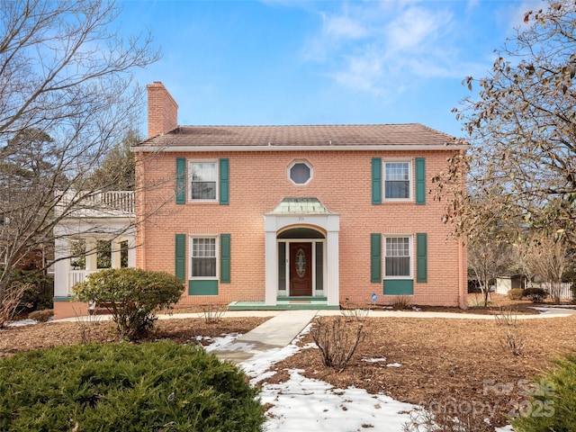 colonial inspired home featuring brick siding and a chimney