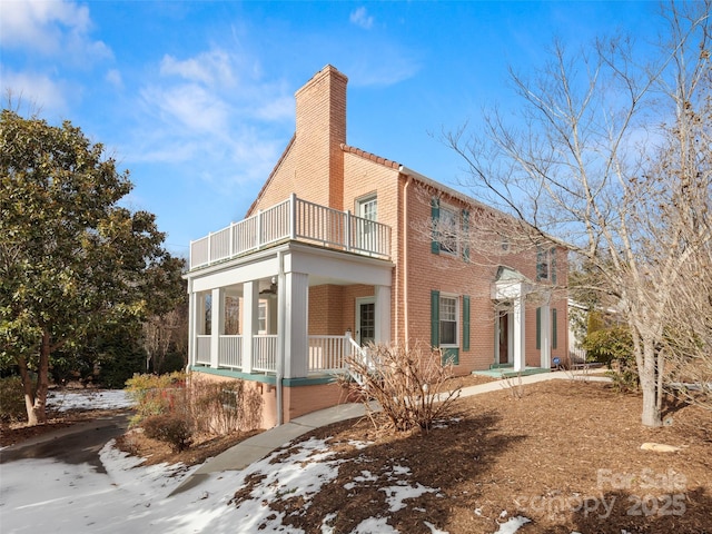 exterior space featuring covered porch, brick siding, a chimney, and a balcony