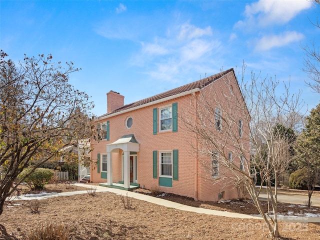 colonial home with brick siding, fence, and a chimney