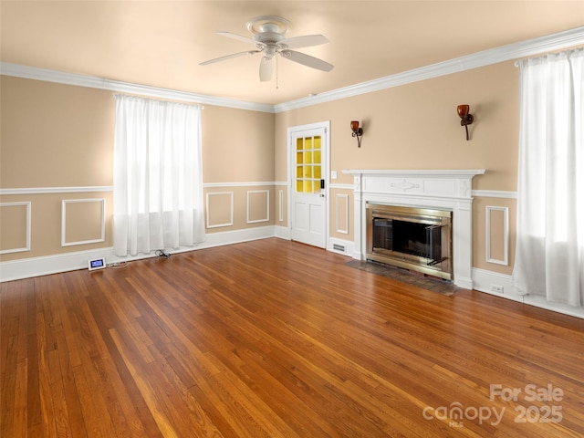 unfurnished living room with a ceiling fan, a fireplace with flush hearth, wood finished floors, crown molding, and a decorative wall