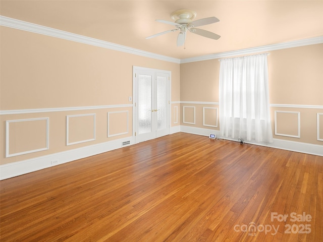 empty room featuring crown molding, wood finished floors, a ceiling fan, and a decorative wall