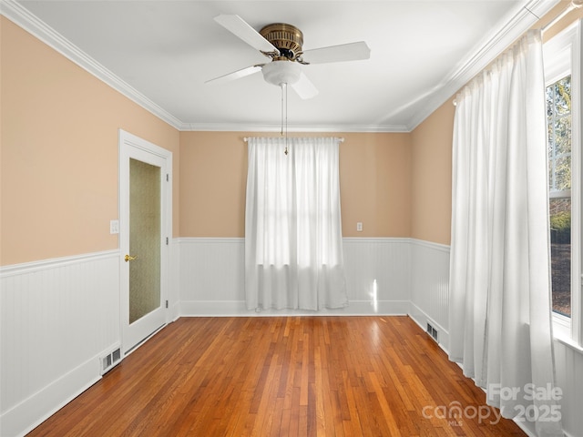 empty room with wainscoting, wood finished floors, visible vents, and crown molding