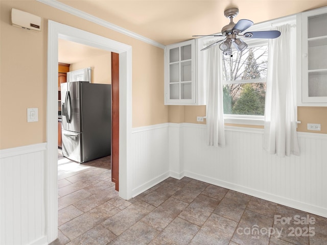 unfurnished dining area with a ceiling fan, an AC wall unit, and wainscoting