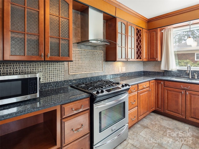 kitchen with stainless steel appliances, a sink, wall chimney range hood, brown cabinets, and glass insert cabinets