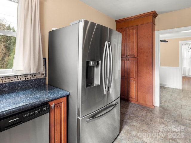 kitchen with a wainscoted wall, stainless steel appliances, visible vents, brown cabinetry, and dark stone countertops