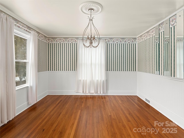 empty room featuring a notable chandelier, a wainscoted wall, plenty of natural light, and wood finished floors