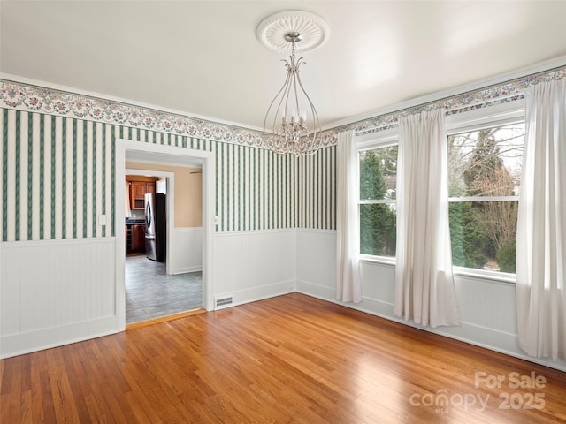 spare room featuring wallpapered walls, a notable chandelier, wood finished floors, and wainscoting