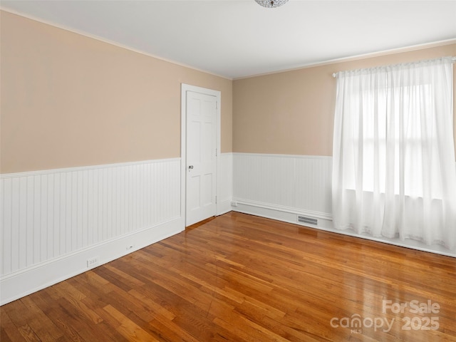 unfurnished room featuring wainscoting, visible vents, and wood finished floors