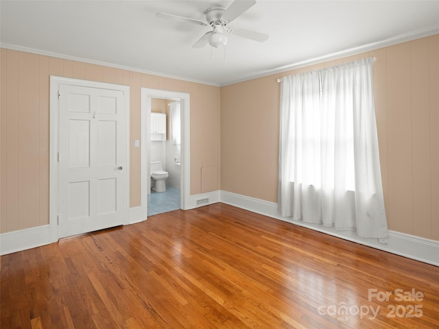 unfurnished bedroom featuring baseboards, ensuite bath, wood finished floors, and crown molding