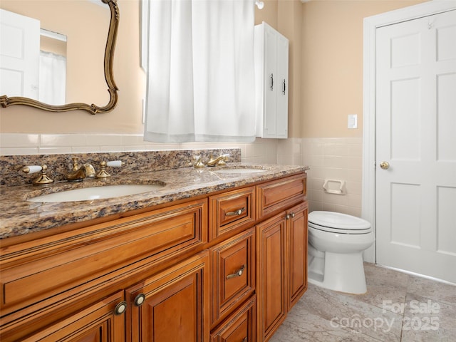 full bath with double vanity, wainscoting, a sink, and tile walls