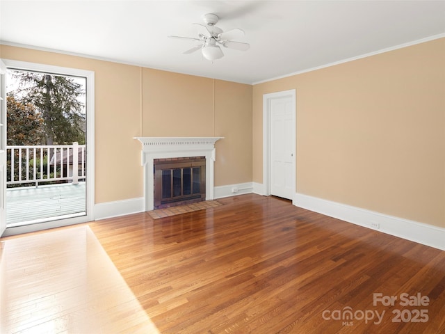 unfurnished living room featuring baseboards, a fireplace with flush hearth, ceiling fan, wood finished floors, and crown molding