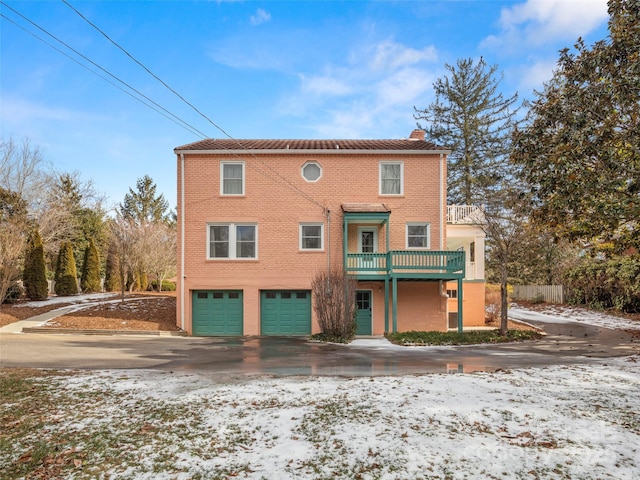 view of front of property with driveway, a garage, a balcony, a chimney, and brick siding