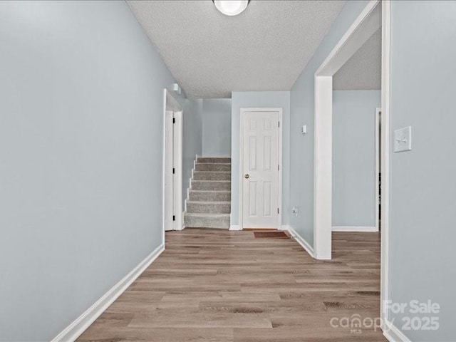 hallway featuring baseboards, a textured ceiling, stairway, and wood finished floors