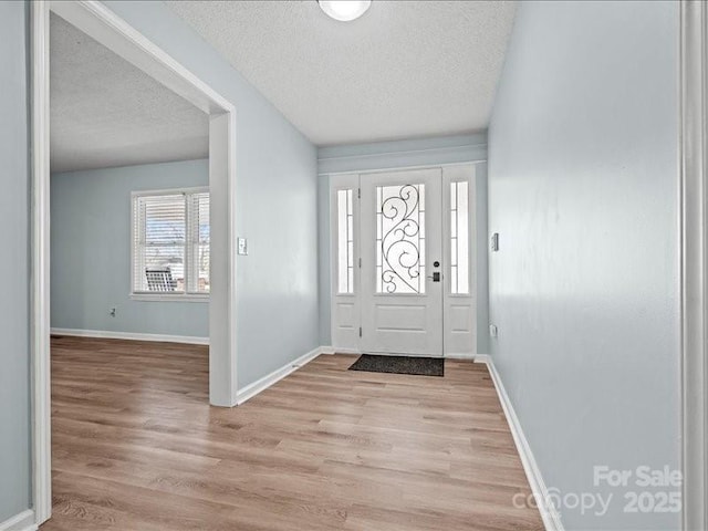 entryway featuring a textured ceiling, light wood-type flooring, and baseboards