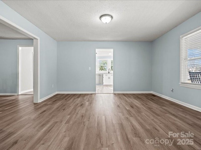 unfurnished room with a textured ceiling, baseboards, and wood finished floors