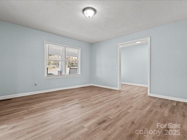 spare room with visible vents, a textured ceiling, baseboards, and wood finished floors