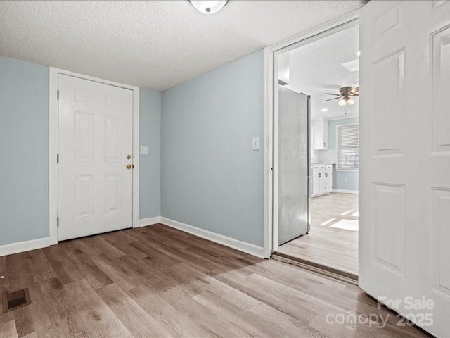 unfurnished room featuring a textured ceiling, wood finished floors, visible vents, and baseboards