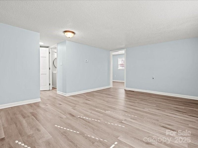 unfurnished room with light wood finished floors, baseboards, and a textured ceiling