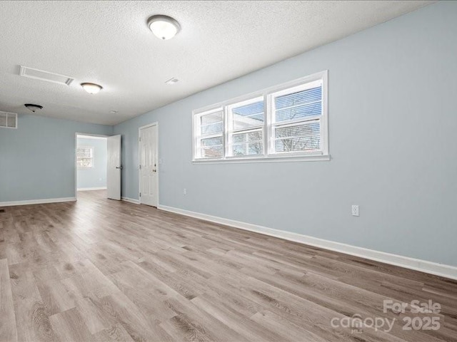 empty room featuring plenty of natural light, a textured ceiling, baseboards, and wood finished floors