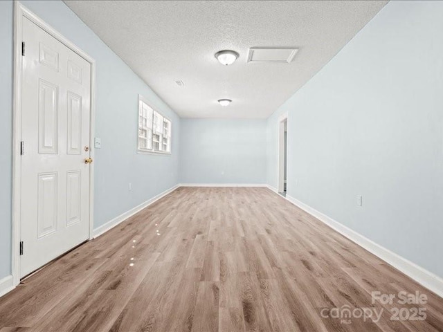 spare room featuring light wood-type flooring, a textured ceiling, and baseboards