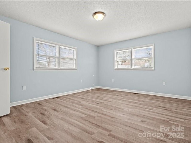 unfurnished room featuring light wood-type flooring, a textured ceiling, and baseboards