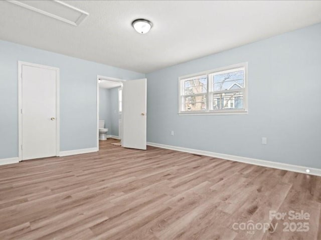 unfurnished bedroom with light wood-type flooring, ensuite bath, attic access, and baseboards