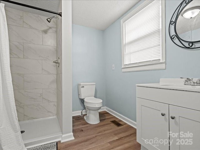 full bathroom with a textured ceiling, toilet, wood finished floors, baseboards, and a shower stall