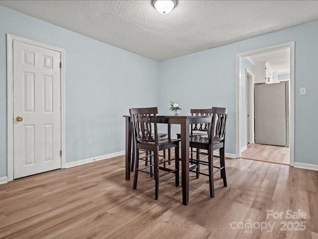 dining space with a textured ceiling, light wood finished floors, and baseboards