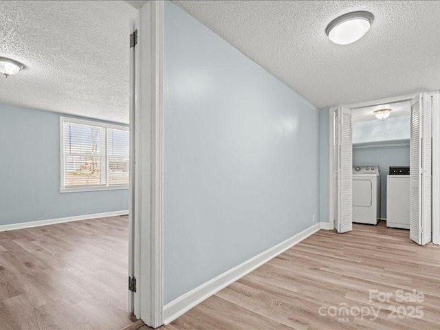 hall featuring a textured ceiling, wood finished floors, washing machine and dryer, and baseboards