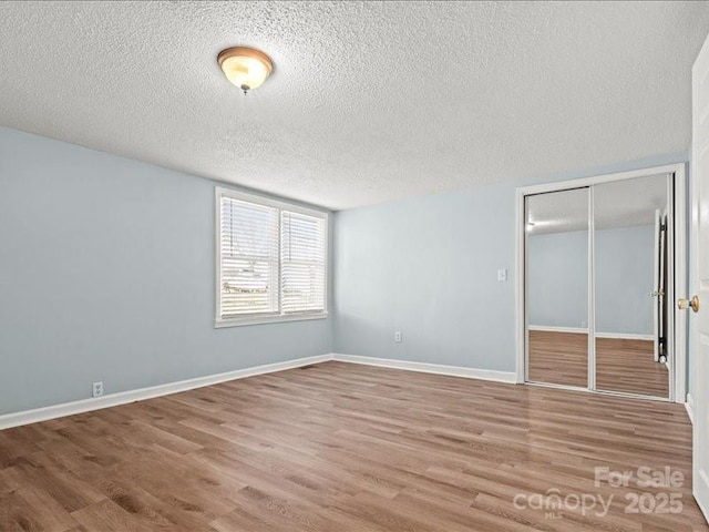 unfurnished bedroom featuring a closet, a textured ceiling, baseboards, and wood finished floors